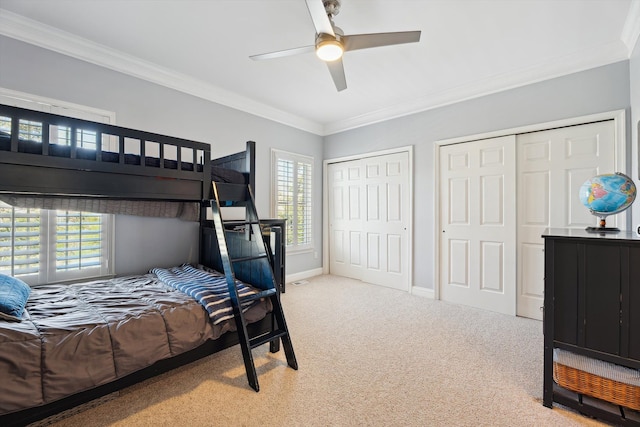 carpeted bedroom with two closets, a ceiling fan, baseboards, and ornamental molding