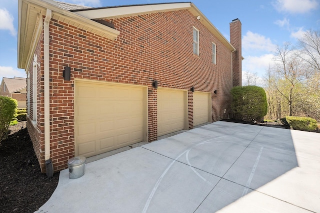 view of home's exterior with brick siding, an attached garage, driveway, and a chimney