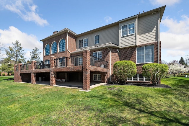 rear view of property with a yard, brick siding, a wooden deck, and a patio area