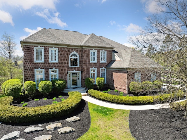 colonial house featuring brick siding and roof with shingles