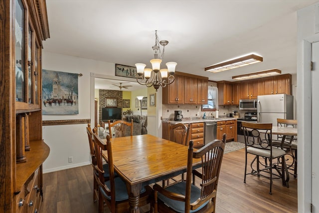dining room with ceiling fan with notable chandelier, baseboards, and dark wood-style floors
