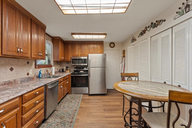 kitchen with brown cabinetry, tasteful backsplash, stainless steel appliances, and light wood-style flooring