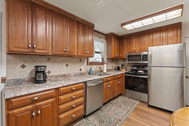 kitchen featuring brown cabinetry, decorative backsplash, stainless steel appliances, and a sink