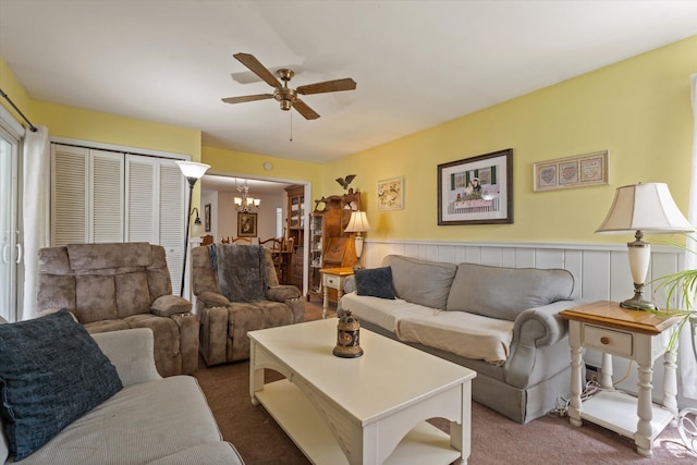 carpeted living area featuring a wainscoted wall and ceiling fan with notable chandelier