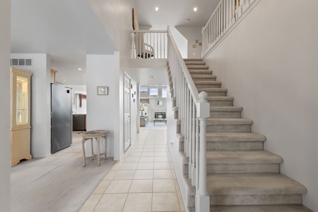staircase with tile patterned floors, a towering ceiling, baseboards, visible vents, and recessed lighting