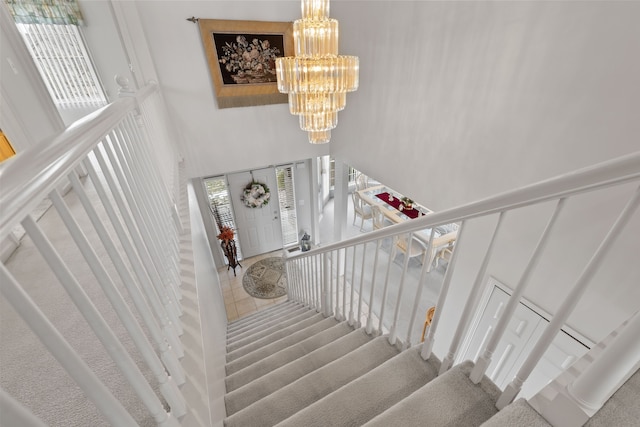 staircase featuring a high ceiling, a notable chandelier, and carpet flooring