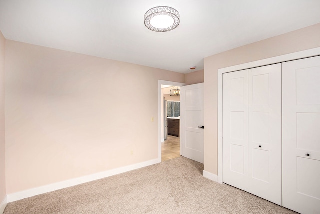 unfurnished bedroom with light carpet, baseboards, and a closet