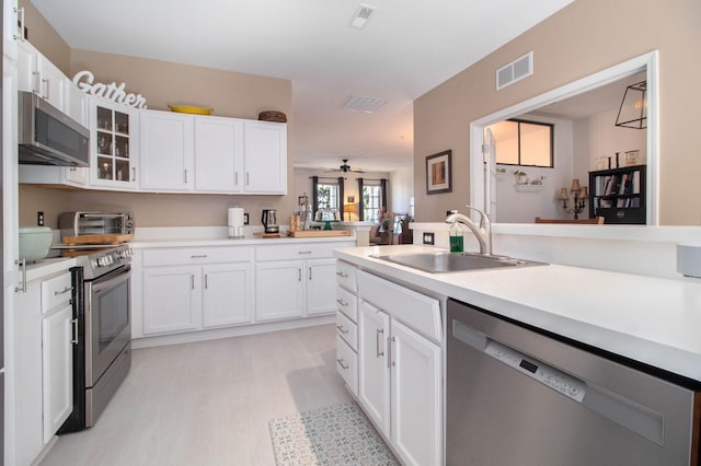 kitchen with a sink, stainless steel appliances, light wood finished floors, white cabinetry, and visible vents