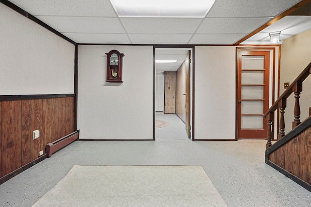 home theater room featuring a baseboard radiator, a drop ceiling, baseboards, wood walls, and wainscoting