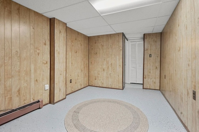 finished below grade area featuring baseboard heating, wood walls, a drop ceiling, and baseboards
