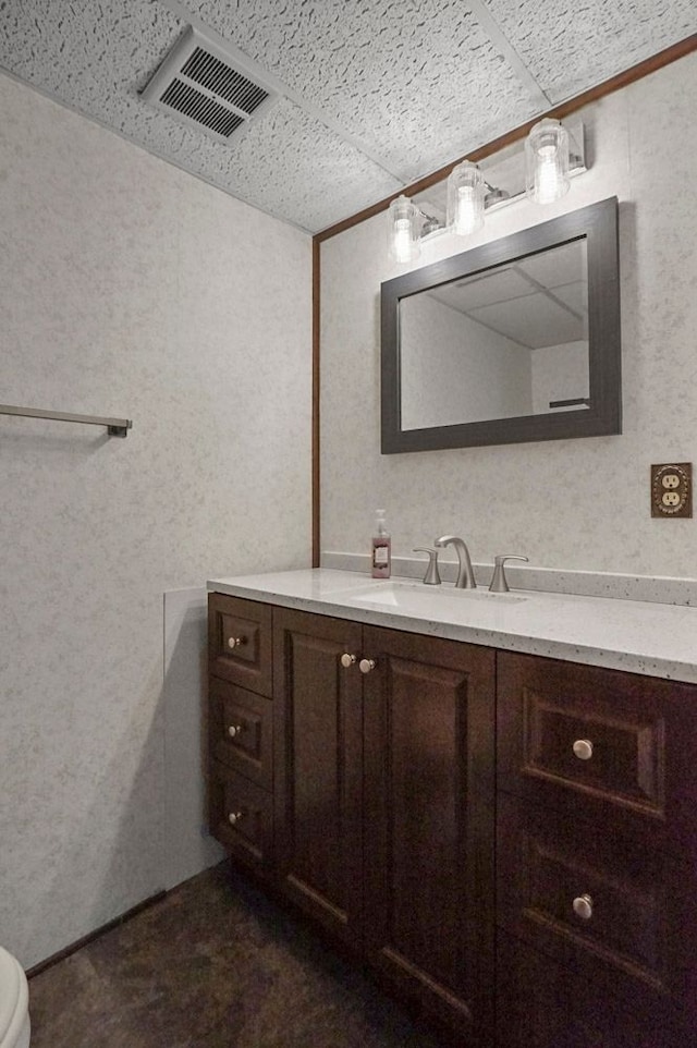bathroom featuring vanity, toilet, a textured wall, and a paneled ceiling