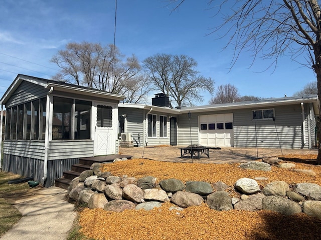 back of house with an attached garage, a sunroom, and a chimney