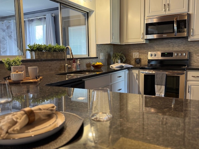 kitchen with white cabinets, a sink, dark stone counters, decorative backsplash, and appliances with stainless steel finishes