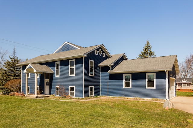 rear view of house with a lawn, a shingled roof, and driveway