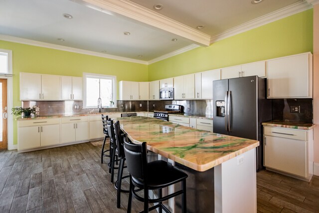 kitchen featuring appliances with stainless steel finishes, dark wood-type flooring, ornamental molding, a kitchen island, and white cabinets
