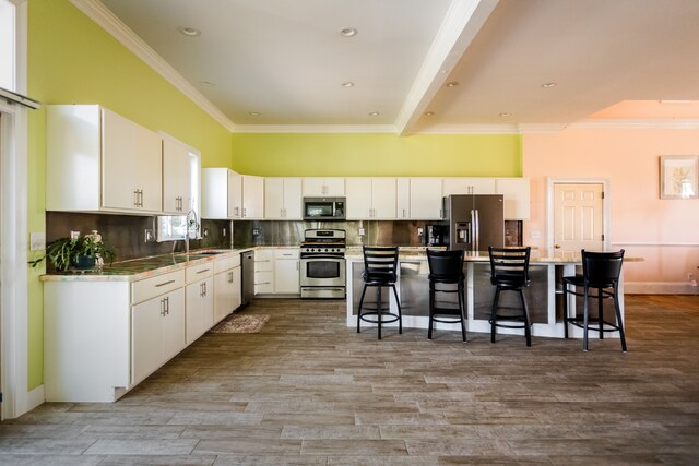 kitchen featuring appliances with stainless steel finishes, a breakfast bar area, crown molding, a center island, and a sink