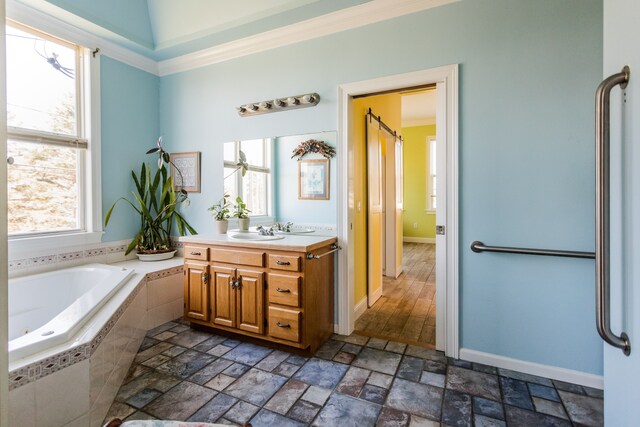 full bath with crown molding, a bath, vanity, stone finish floors, and baseboards