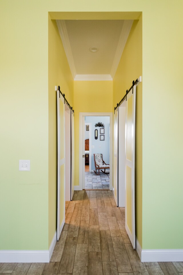 corridor featuring a barn door, ornamental molding, and baseboards