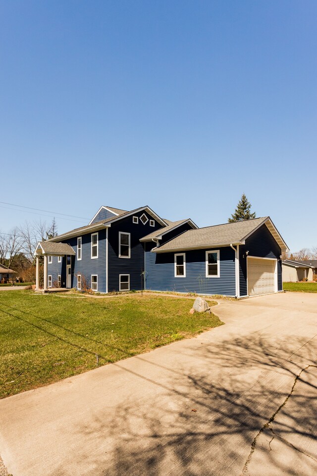 split level home featuring driveway, an attached garage, and a front lawn