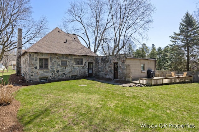 back of property featuring a wooden deck, stone siding, fence, and a yard