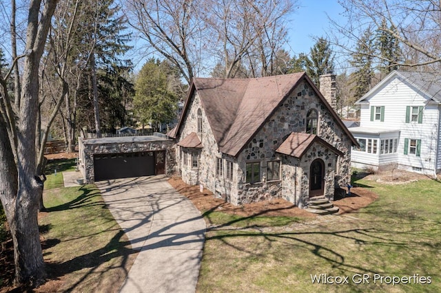 tudor-style house featuring stone siding, entry steps, aphalt driveway, and a garage
