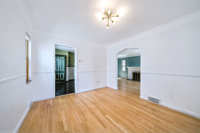 spare room with light wood-style floors, arched walkways, baseboards, a fireplace with flush hearth, and visible vents
