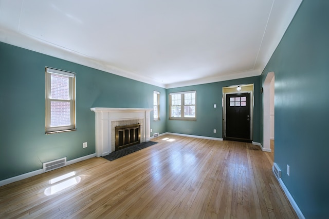 unfurnished living room featuring baseboards, visible vents, a fireplace with flush hearth, and wood finished floors