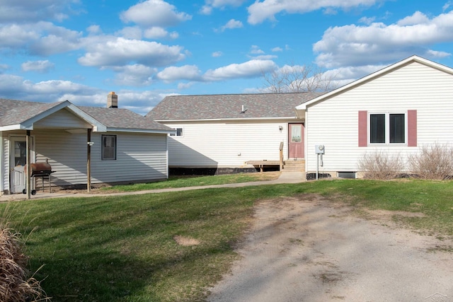 rear view of property featuring a lawn, a shingled roof, and entry steps