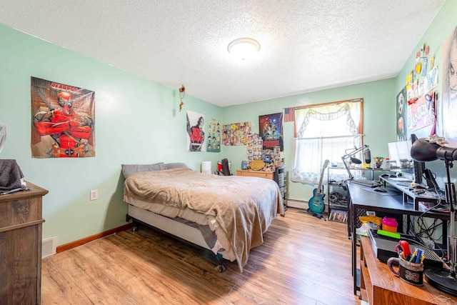 bedroom featuring a baseboard heating unit, wood finished floors, a textured ceiling, and visible vents