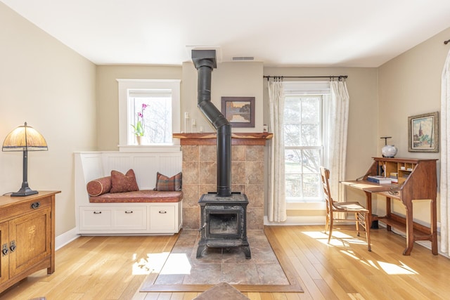 living area featuring a healthy amount of sunlight, a wood stove, light wood-style floors, and visible vents