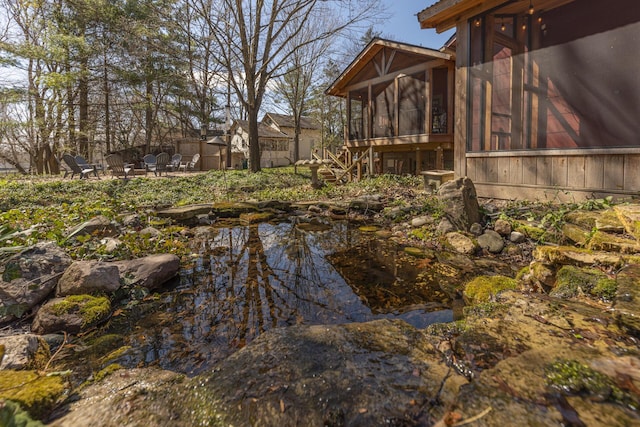 view of yard with a small pond, stairs, a sunroom, a patio, and an outdoor fire pit