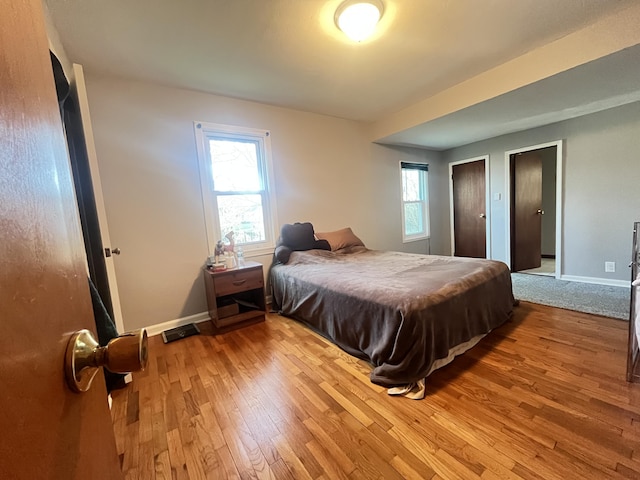 bedroom with hardwood / wood-style flooring, baseboards, and two closets