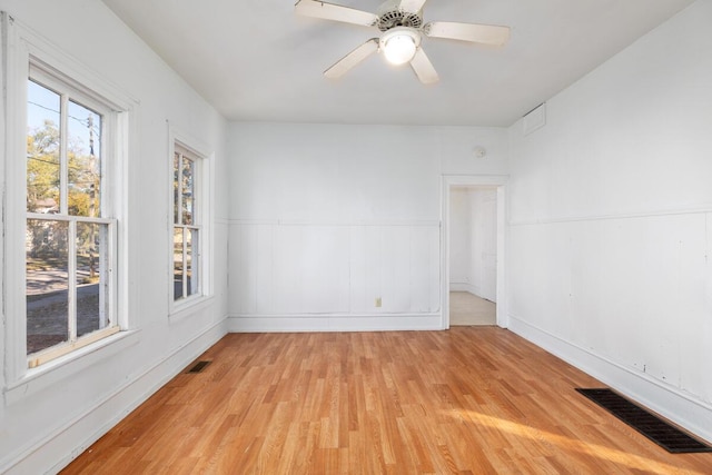 unfurnished room featuring light wood-style floors, visible vents, ceiling fan, and wainscoting