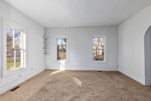 unfurnished room with carpet floors, arched walkways, a healthy amount of sunlight, and visible vents