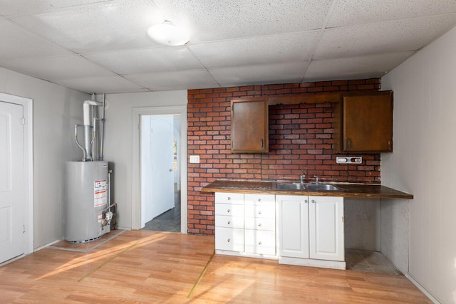 interior space with light wood-style flooring, a sink, gas water heater, a drop ceiling, and dark countertops