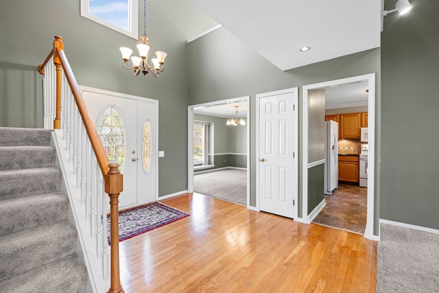 foyer with light wood-style floors, a towering ceiling, baseboards, an inviting chandelier, and stairs