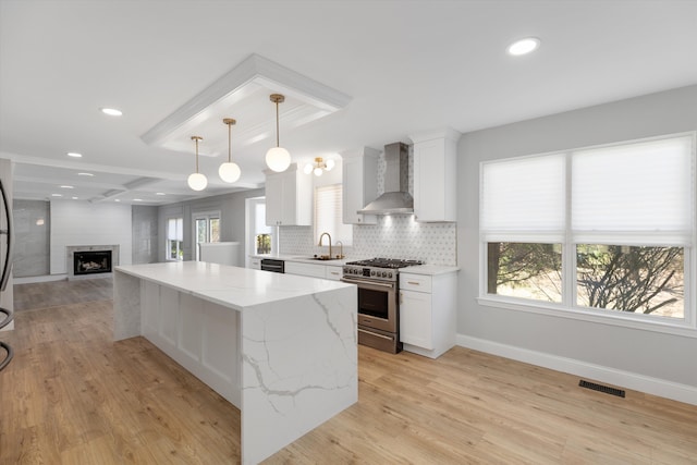 kitchen with white cabinets, visible vents, a sink, wall chimney exhaust hood, and stainless steel range