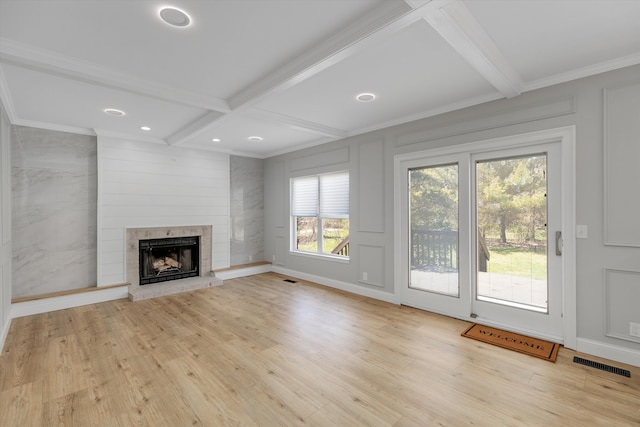 unfurnished living room featuring a fireplace with raised hearth, light wood-style flooring, visible vents, and beam ceiling