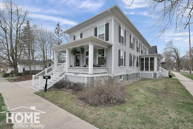 view of front facade featuring stairway, a sunroom, covered porch, and a front yard
