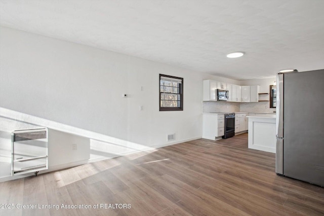 unfurnished living room with wood finished floors, baseboards, and heating unit