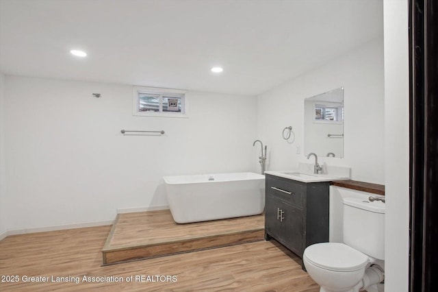 bathroom with wood finished floors, vanity, a freestanding bath, toilet, and recessed lighting