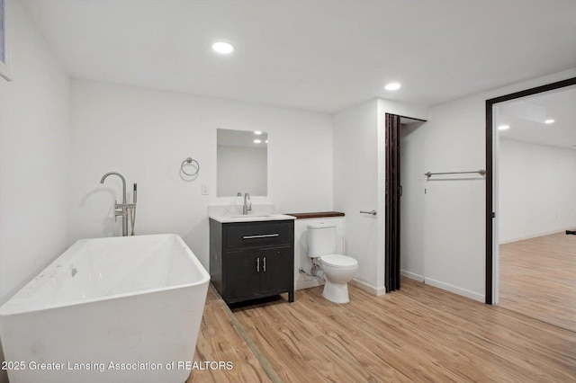 bathroom with recessed lighting, wood finished floors, a soaking tub, and vanity