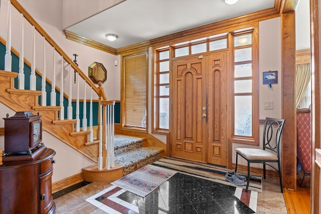 foyer entrance with baseboards, crown molding, stairs, and a wainscoted wall