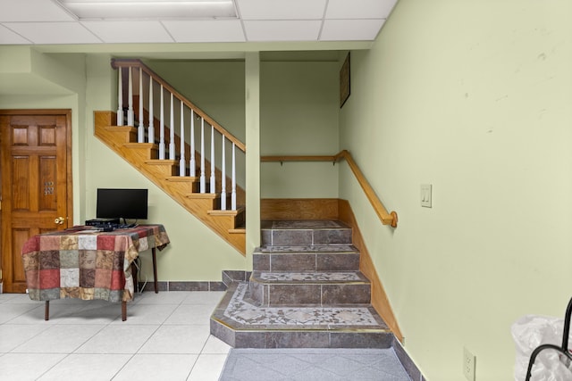 stairs featuring baseboards, tile patterned flooring, and a drop ceiling