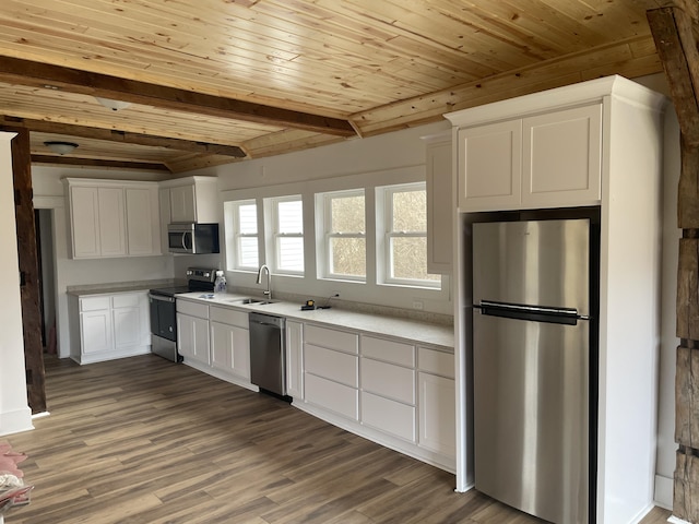 kitchen featuring wood finished floors, stainless steel appliances, light countertops, white cabinetry, and beam ceiling