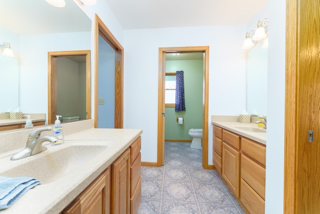 bathroom with two vanities, toilet, baseboards, and a sink