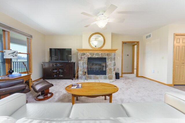 carpeted living room featuring ceiling fan, baseboards, a stone fireplace, and visible vents