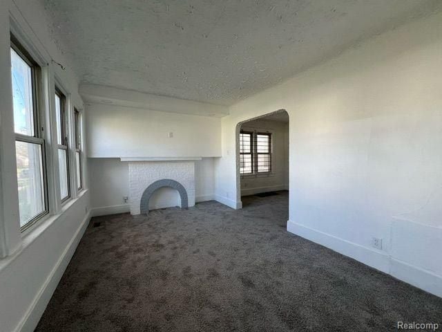 unfurnished living room with a brick fireplace, arched walkways, baseboards, a textured ceiling, and carpet flooring