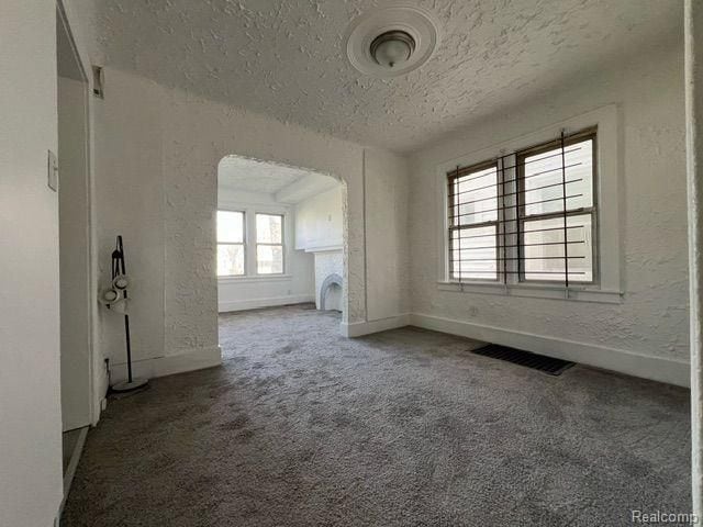 unfurnished room featuring visible vents, arched walkways, carpet floors, baseboards, and a textured ceiling