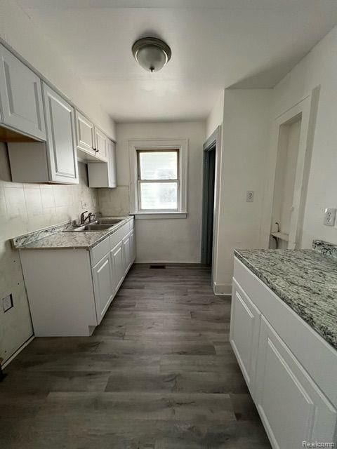 kitchen with white cabinets, decorative backsplash, a sink, and dark wood-style floors